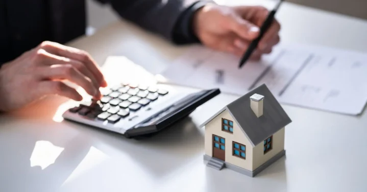 Pessoa usando calculadora com modelo de casa ao lado - artigo sobre ITBI e valor de mercado na compra de imóveis